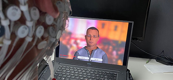 This image shows a subject with electrodes attached to their head watching a character on a computer screen.
