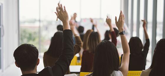 The image shows several people raising their hands for a vote.