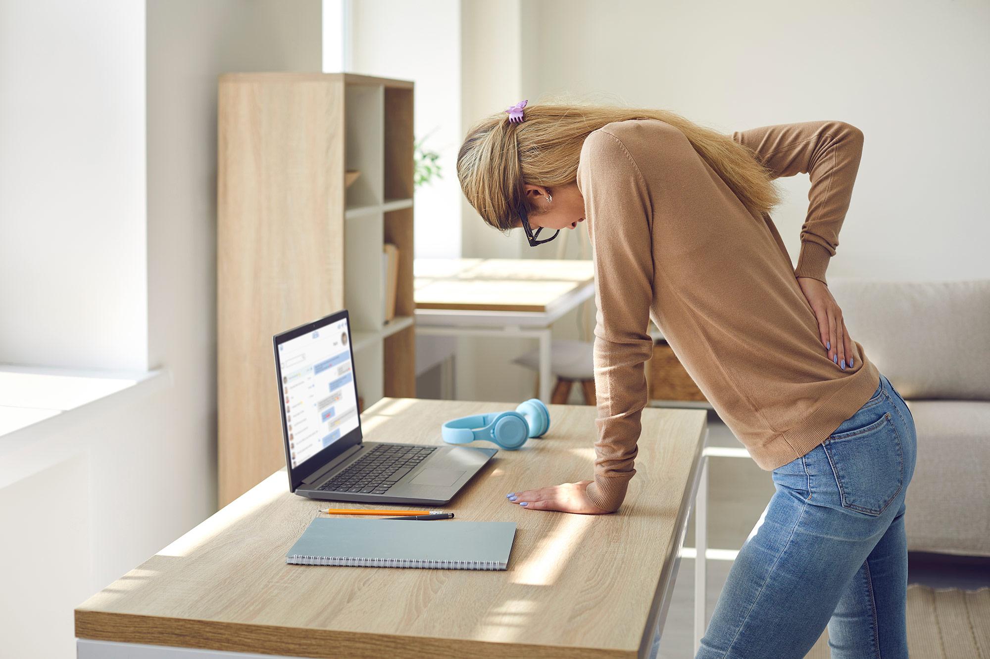 A woman with back pain stands at her office desk.