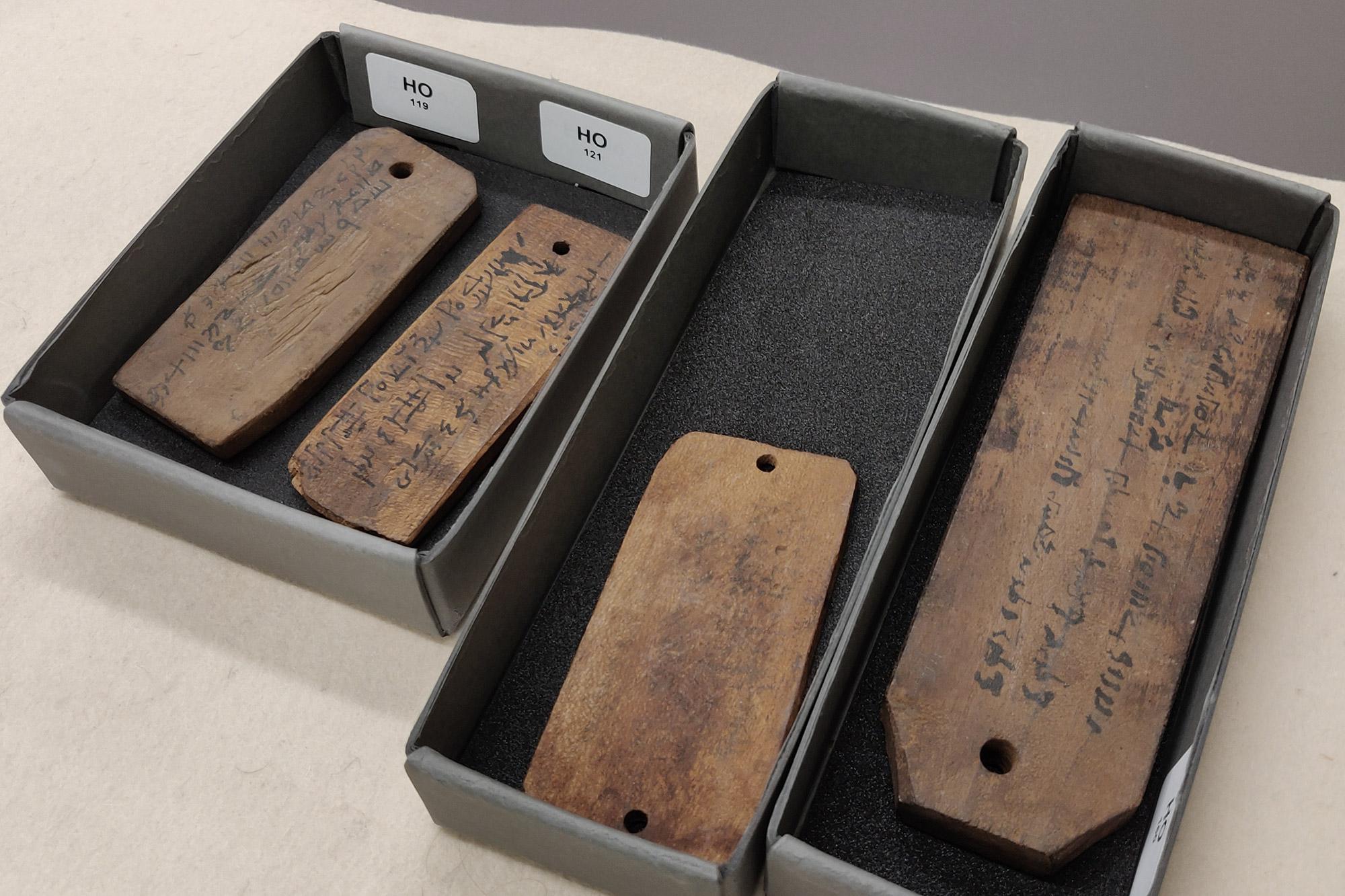 Mehrere Holzetiketten von Mumien, die in zwei Schachteln aufgereiht sind.