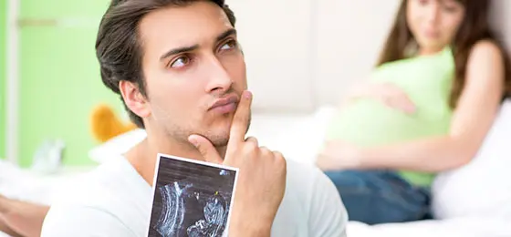 A man is holding an ultrasound image of his child while looking thoughtfully towards the top right.