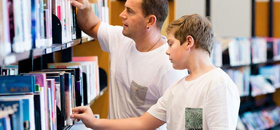 A boy and his father searching for books in the library.